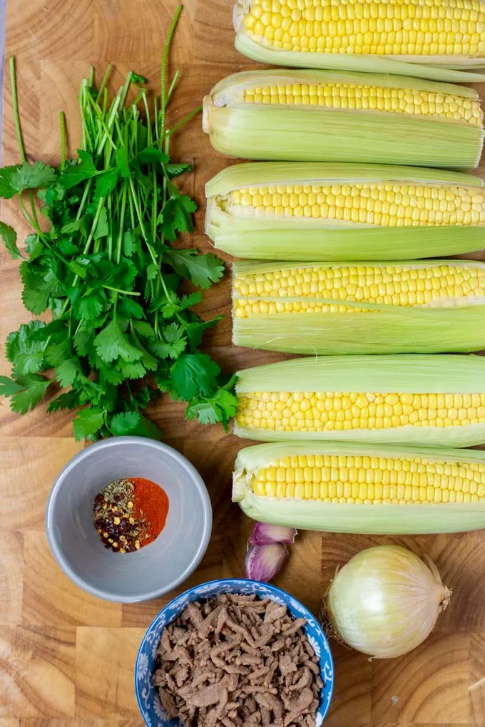 Ingredients needed for making Fried Corn are collected on a wooden board.