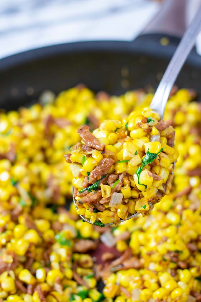 A large spoon of Fried Corn is lifted from the pan.