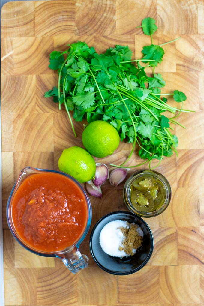 Ingredients needed for making the Restaurant Style Salsa are collected on a wooden board.