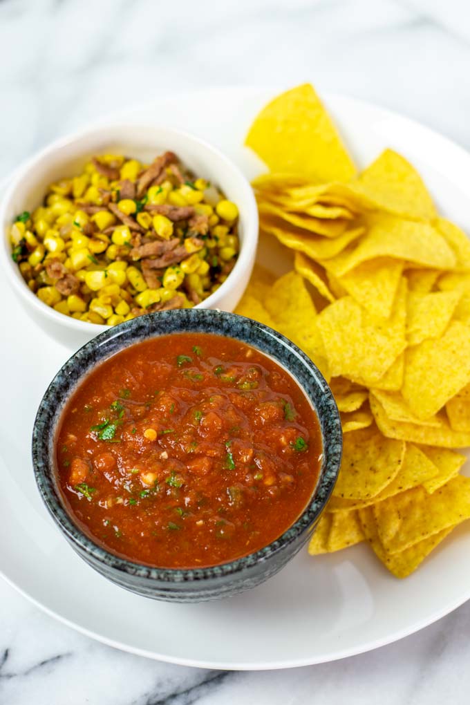 A small serving bowl of salsa on a plate, served with fried corn and chips.