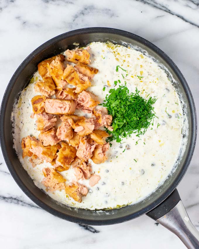 Top view of a saucepan with the pulled salmon being added to the base sauce.