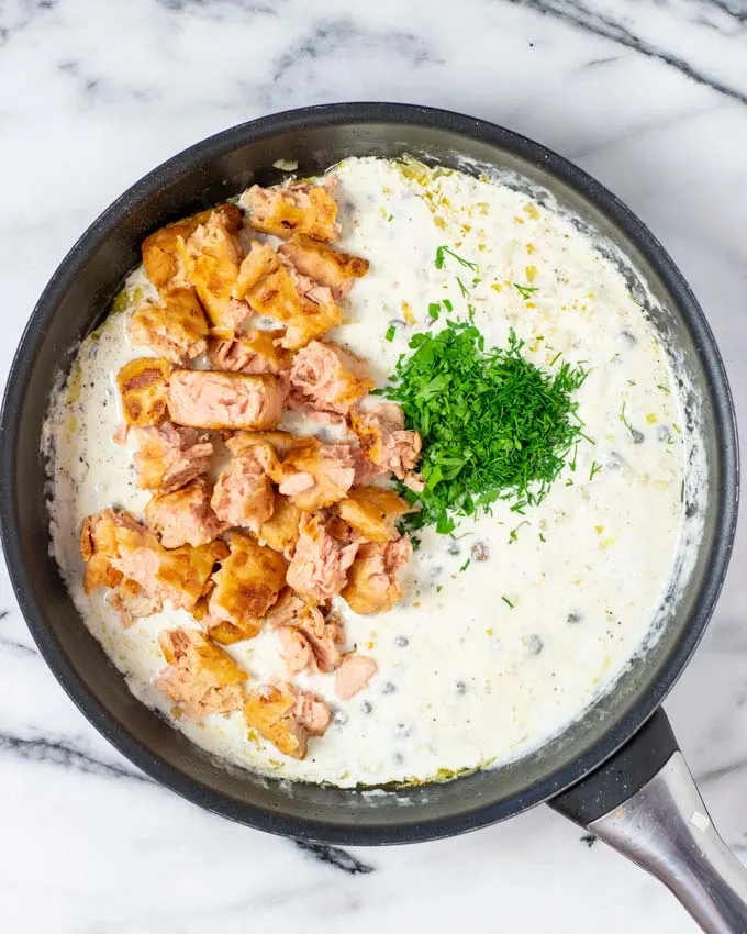 Top view of a saucepan with the pulled salmon being added to the base sauce.