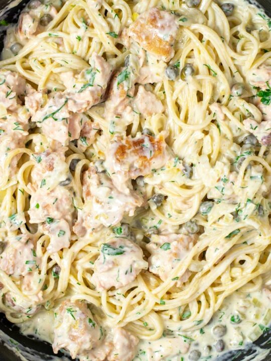 Closeup of the cream Salmon Pasta with salmon bits, fresh herbs, capers visible.