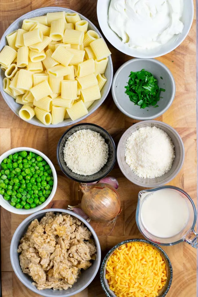 Ingredients needed to make Tuna Noodle Casserole are collected on a wooden board.
