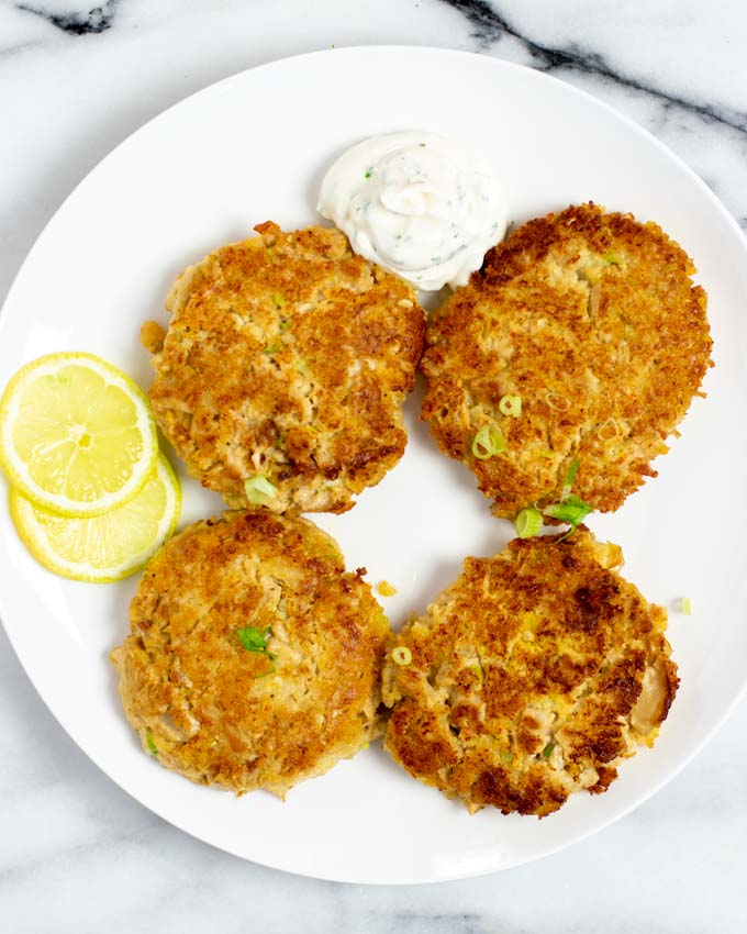 Four Tuna Patties are served on a plate with some dipping sauce.