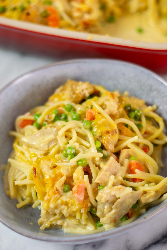 Closeup of a portion of the Chicken Noodle Casserole in a bowl with the casserole dish in the background.