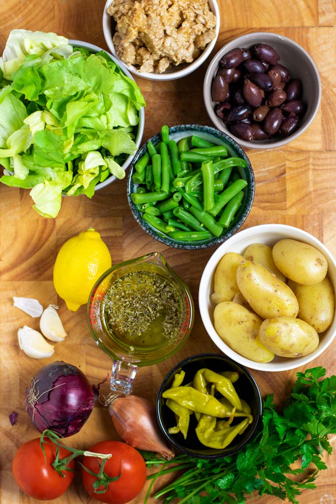 Ingredients needed to make Nicoise Salad are assembled on a wooden board.