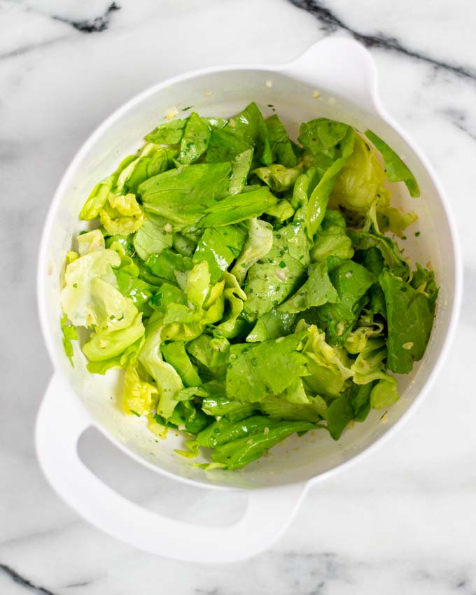 A mixing bowl with green salad, mixed with dressing.