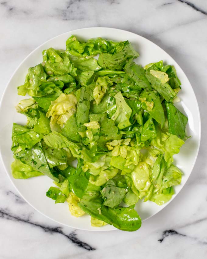 Green salad with dressing is placed on a white plate.