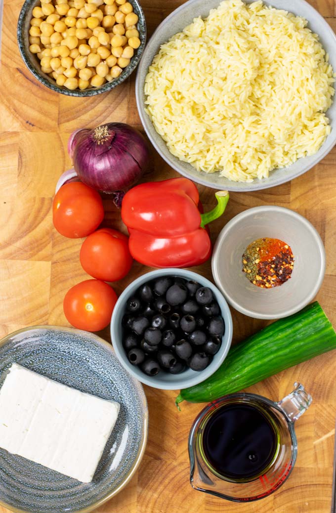 Ingredients needed for making the Orzo Salad are collected on a wooden board.