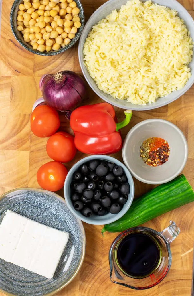 Ingredients needed for making the Orzo Salad are collected on a wooden board.