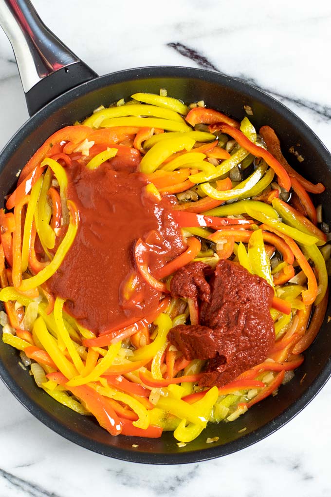 Top view on a pan with the sweet pepper and onion, with tomato paste and sauce being added.
