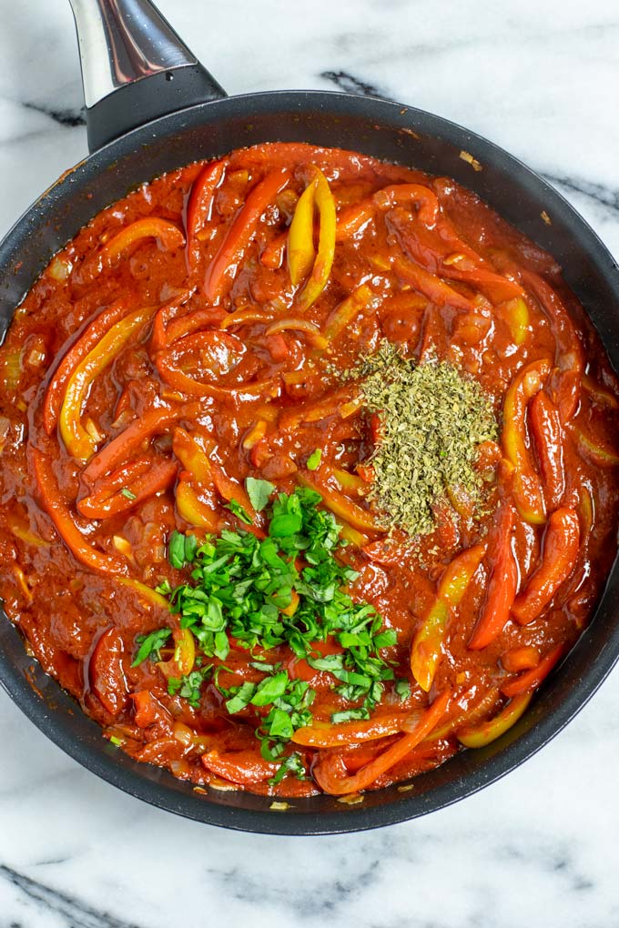 Top view on the pan with the Peperonata, showing how herbs are added to the dish.