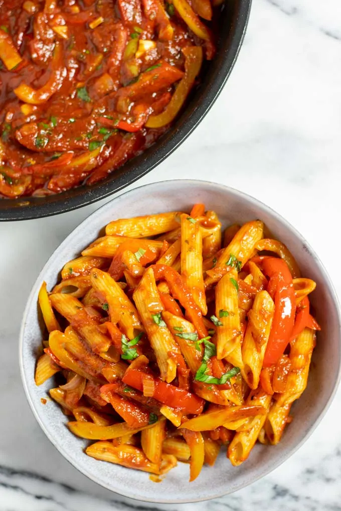 Top view on a portion of the Peperonata served with pasta, with the pan in the background.