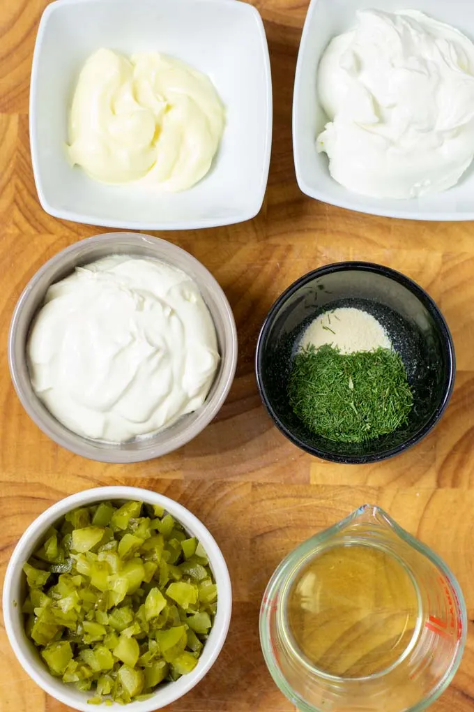 Ingredients needed to make Pickle Dip are collected on a wooded board.