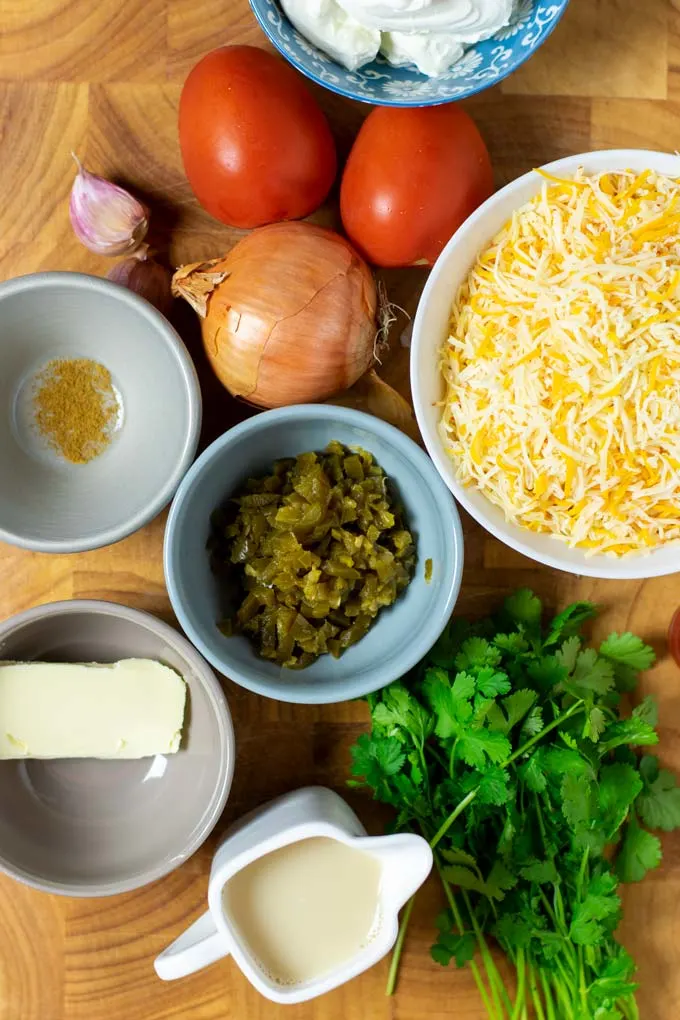 Ingredients needed to make the Queso Dip are collected on a wooden board.