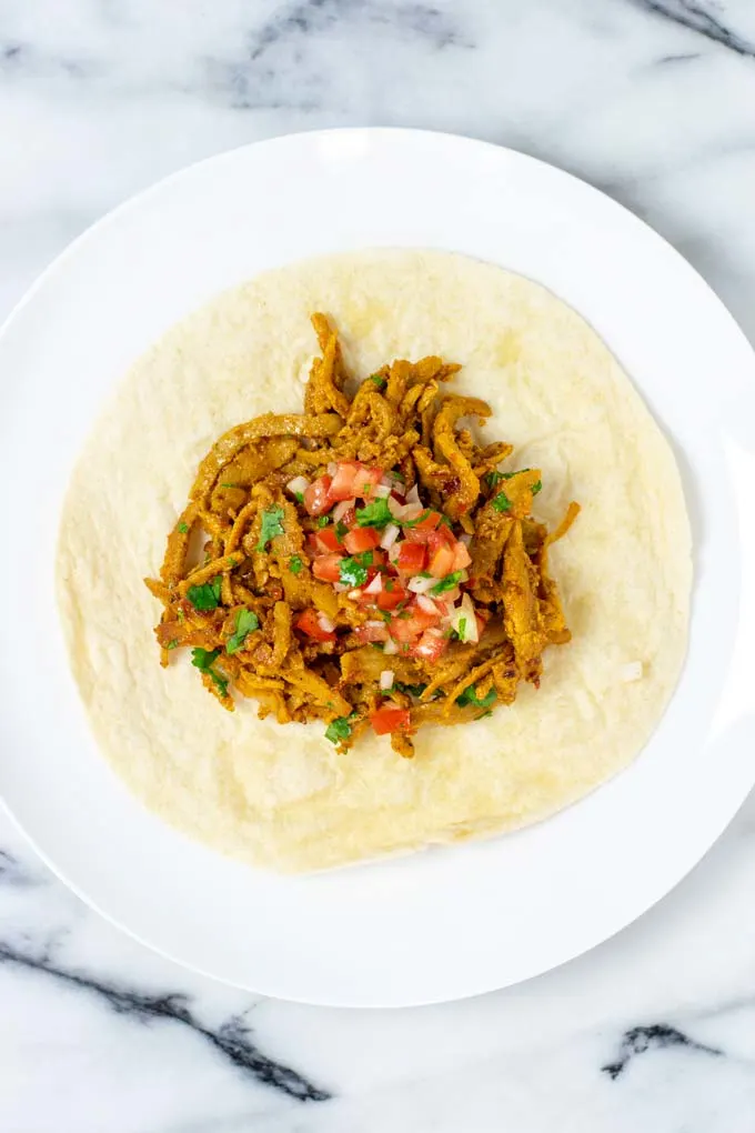 Top view on a plate with Barbacoa served on a tortilla and topped with fresh salsa.