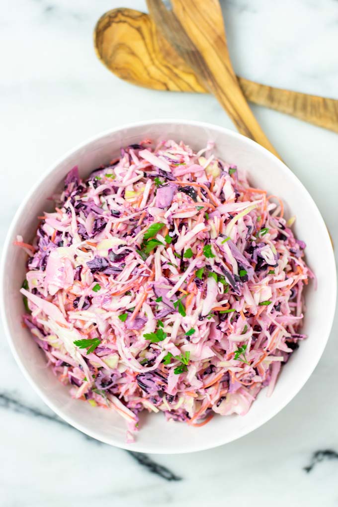 Top view on a white serving bowl with the Coleslaw, with salad cutlery in the background.