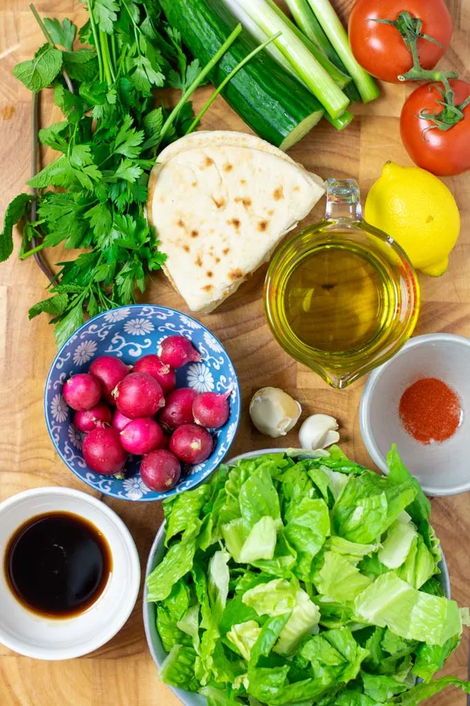 Ingredients needed to make Fattoush Salad are collected on a wooden board.