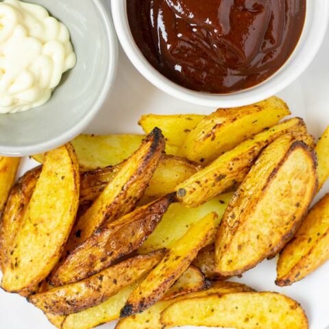 A serving of the Potato Wedges on a plate with mayo and ketchup.
