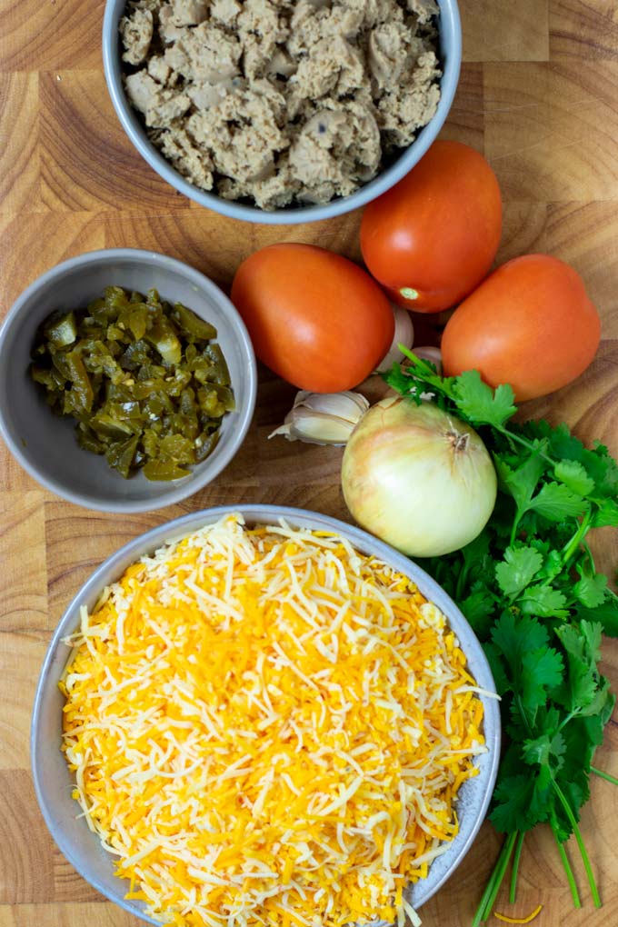 Ingredients needed for making Queso Fundido are collected on a wooden board.