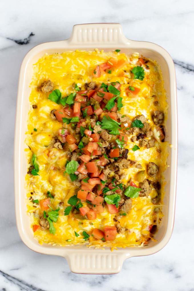 Top view on a casserole with the Queso Fundido after baking, garnished with extra salsa and sausage.