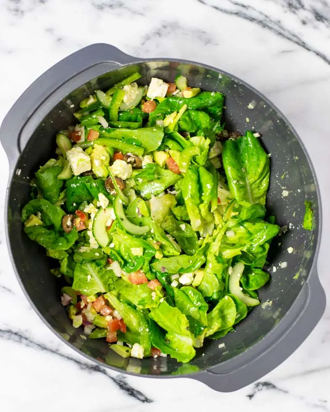 Top view of a large mixing bowl with the green salad ingredients having been mixed with the dressing.