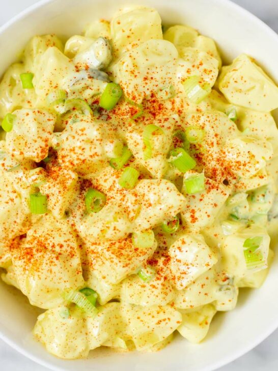 Closeup view on potatoes, pickles, celery, and scallions in a creamy dressing.