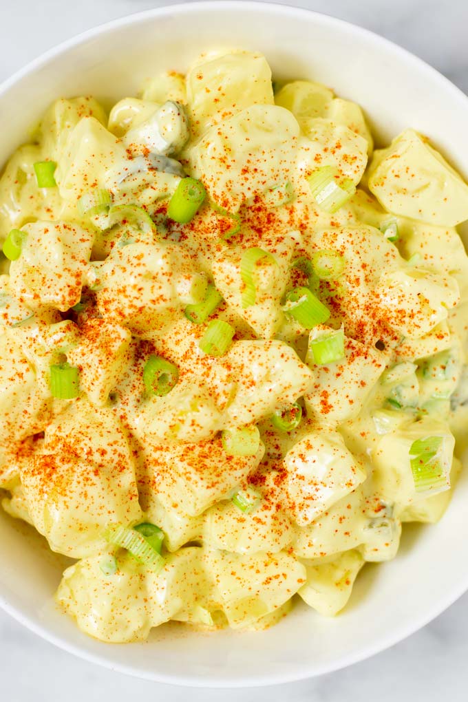 Closeup view on potatoes, pickles, celery, and scallions in a creamy dressing.