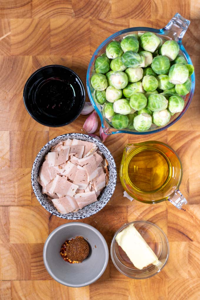 Ingredients needed for Bacon Brussels Sprouts are collected on a wooden board.
