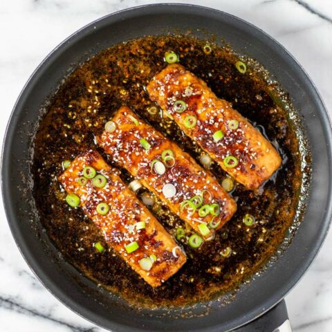 Top view of Teriyaki Salmon in a pan, garnished with scallions and sesame.