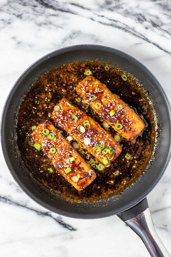 Top view of Teriyaki Salmon in a pan, garnished with scallions and sesame.