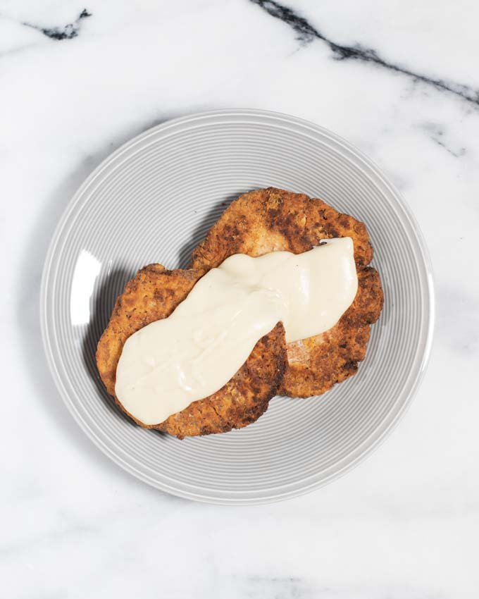 Two Country Fried Steaks are served on a plate with some gravy.