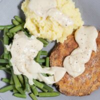 A serving of Country Fried Steak with mashed potatoes and green beans.