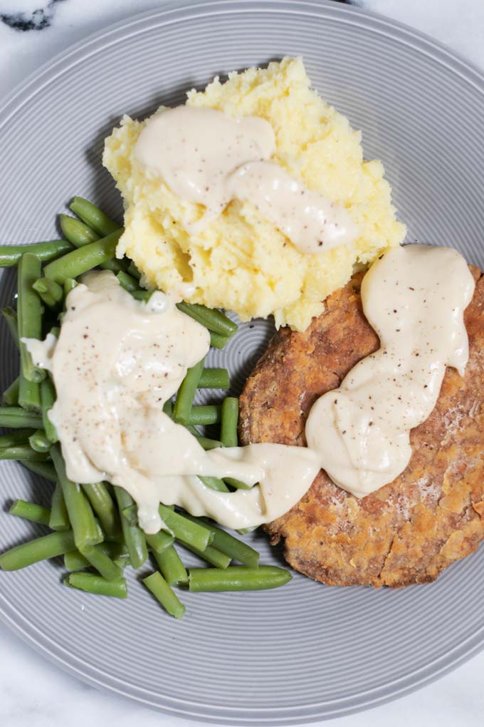 A serving of Country Fried Steak with mashed potatoes and green beans.