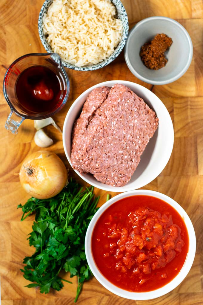 Ingredients needed for making Porcupine Meatballs are collected on a wooden board.