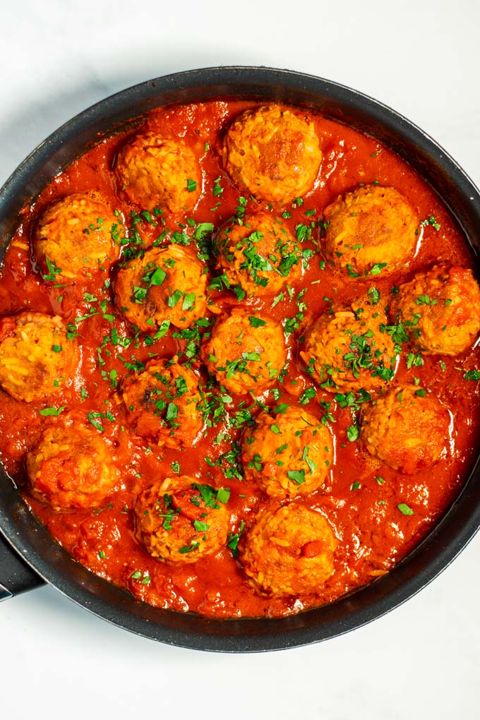 Top view of a frying pan with Porcupine Meatballs in tomato sauce, garnished with fresh parsley.