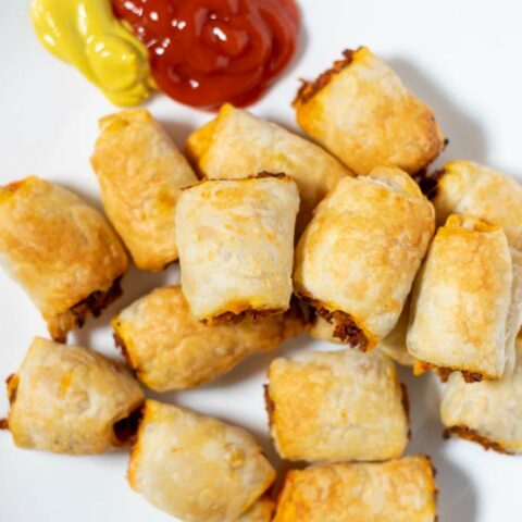 Sausage Rolls on a serving plate, with ketchup and mustard as sides.