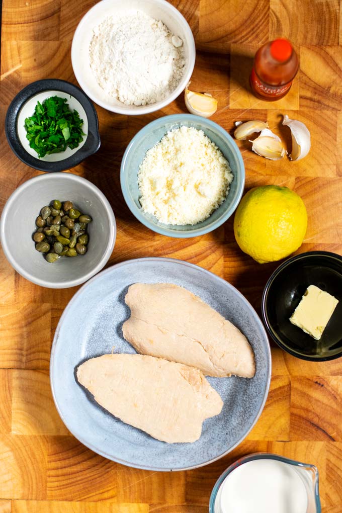 Ingredients needed to make Chicken Piccata are collected on a wooden board.