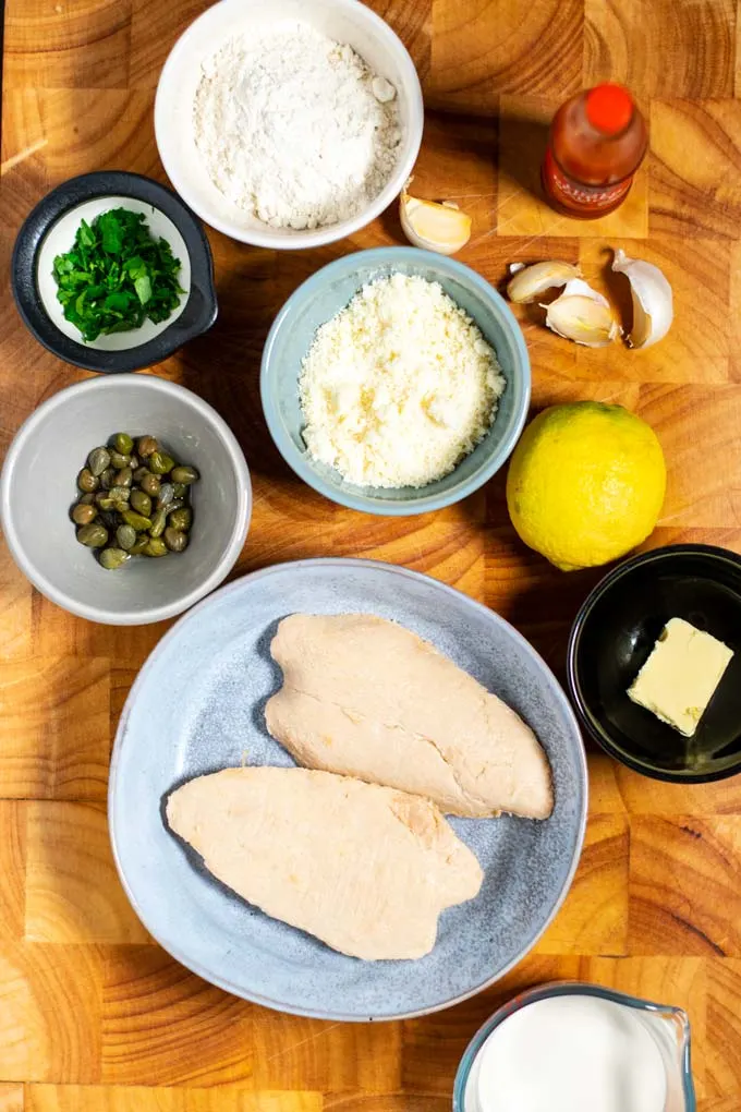 Ingredients needed to make Chicken Piccata are collected on a wooden board.