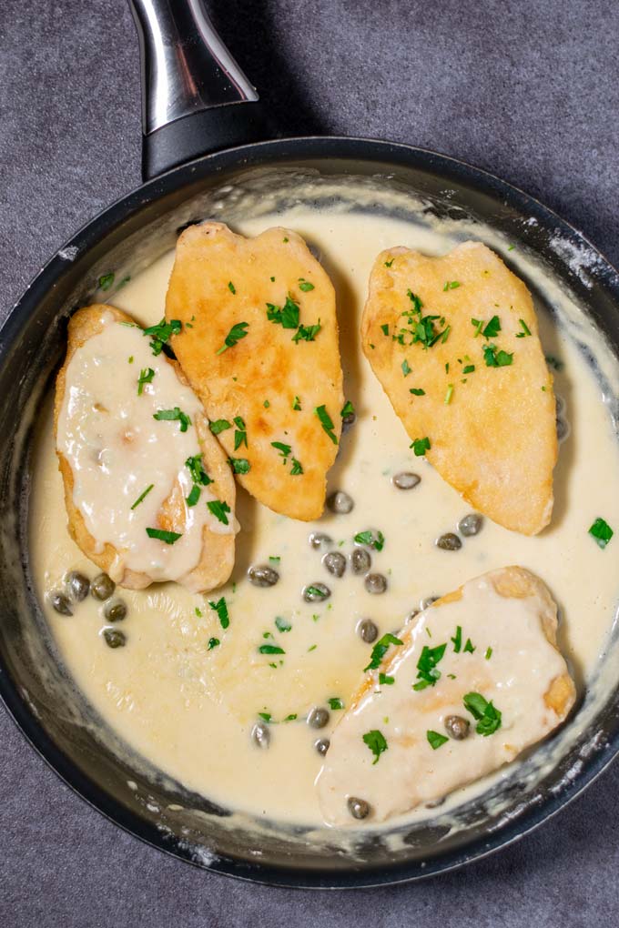 Top view of the ready Chicken Piccata. Four vegan chicken breasts in creamy sauce, garnished with parsley.