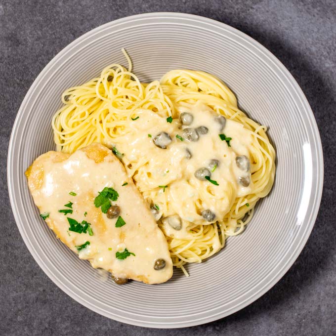 Top view on a serving of Chicken Piccata with spaghetti on a plate.