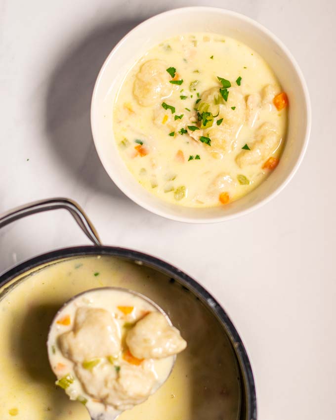 A portion of Chicken and Dumplings in a small serving bowl with the pot and a large spoon in the background.