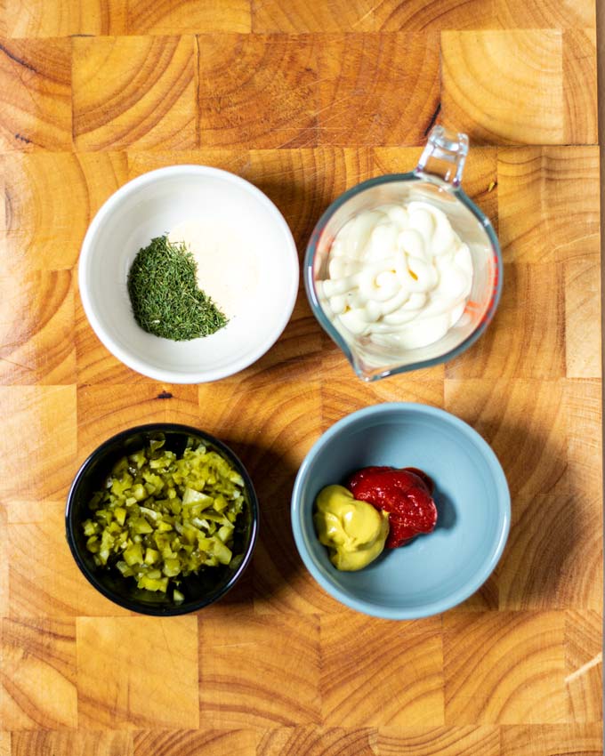 Ingredients needed to make Hot Dog Sauce assembled in four small bowls on a wooden board.