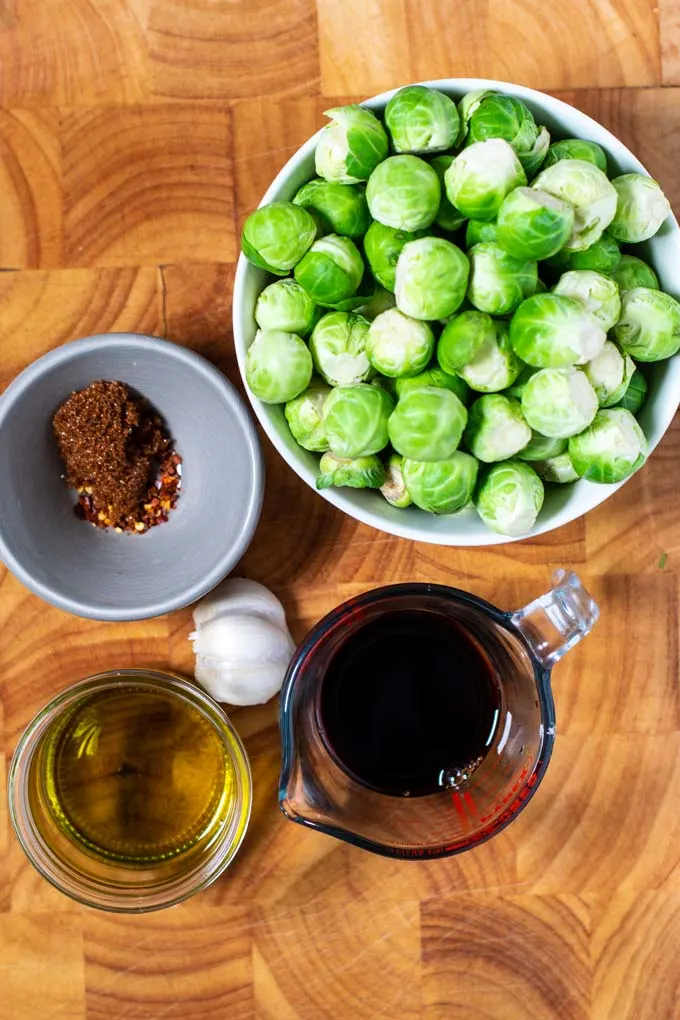 Ingredients for making Roasted Brussels Sprouts are assembled on a wooden board.