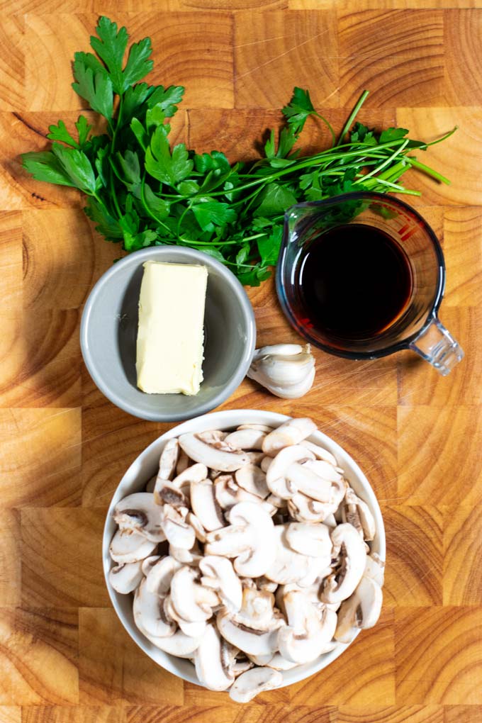 Ingredients needed to make Sautéed Mushrooms are collected on a wooden board.