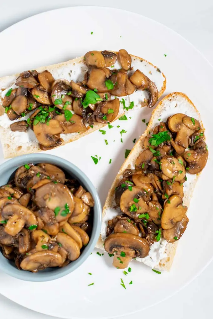 Top view of a plate with two sandwiches served with Sautéed Mushrooms.