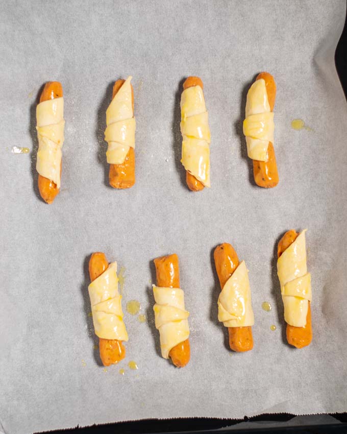 Top view on a baking sheet with eight unbaked Pigs in a Blanket.