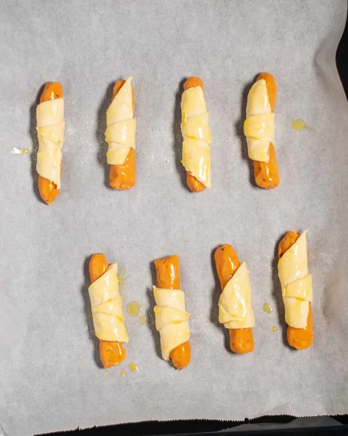 Top view on a baking sheet with eight unbaked Pigs in a Blanket.