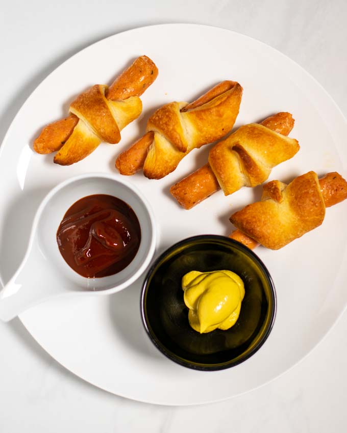 Top view on a plate with four Pigs in a Blanket, served with ketchup and mustard.